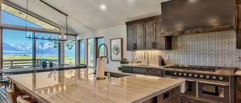 A modern kitchen with a large island, stainless steel appliances, and a view of mountains.