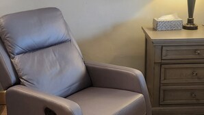 Una silla reclinable, una lámpara, un caja y un cuadro en la pared.