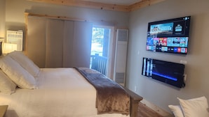 Habitación de hotel con cama, televisor montado en la pared y ventana con cortinas.