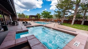 Una piscina rectangular con muelle de madera y sillas de descanso, rodeada por una valla de madera y árboles.