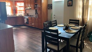 A kitchen with wooden cabinets, a dining table set for four, and a large window with curtains. - 🏝️ TAG Paradise Vacation Home | 1BR • A/C • Free Wi-Fi • Near Mero Beach (Roseau)