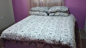 A bedroom with a bed, purple walls, and a window with sheer curtains. - 🏝️ TAG Paradise Vacation Home | 1BR • A/C • Free Wi-Fi • Near Mero Beach (Roseau)