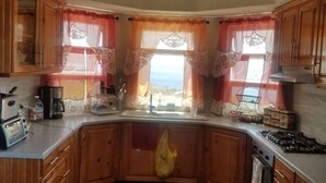 A kitchen with wooden cabinets, a gas stove, a coffee maker, and a window with floral curtains. - 🏝️ TAG Paradise Vacation Home | 1BR • A/C • Free Wi-Fi • Near Mero Beach (Roseau)