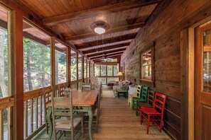 Une cabane en bois comprenant un coin repas, de grandes fenêtres et un ventilateur de plafond.