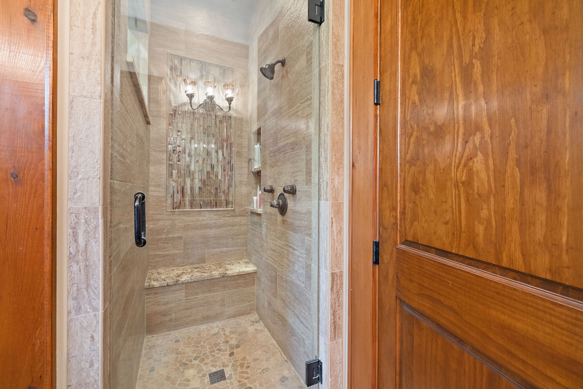 A shower area with a glass door, a bench, and a tiled floor.