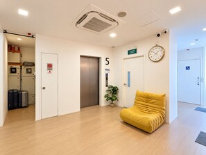 Un hall d’hôtel avec un ascenseur, un canapé jaune, une horloge et une porte accessible aux personnes en fauteuil roulant.