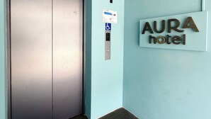 An elevator door with a sign above it and a wall sign that reads 'AURA hotel'. - Aura Hotel Mackenzie (Singapore)