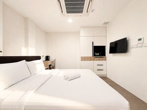 Une chambre d’hôtel équipée d’un lit, d’un bureau, d’une télévision et d’un panneau de commande fixé au mur.