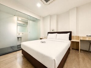 A modern hotel room with a large bed, a bedside table, a desk, and a glass partition separating the room from the bathroom. - Aura Hotel Mackenzie (Singapore)
