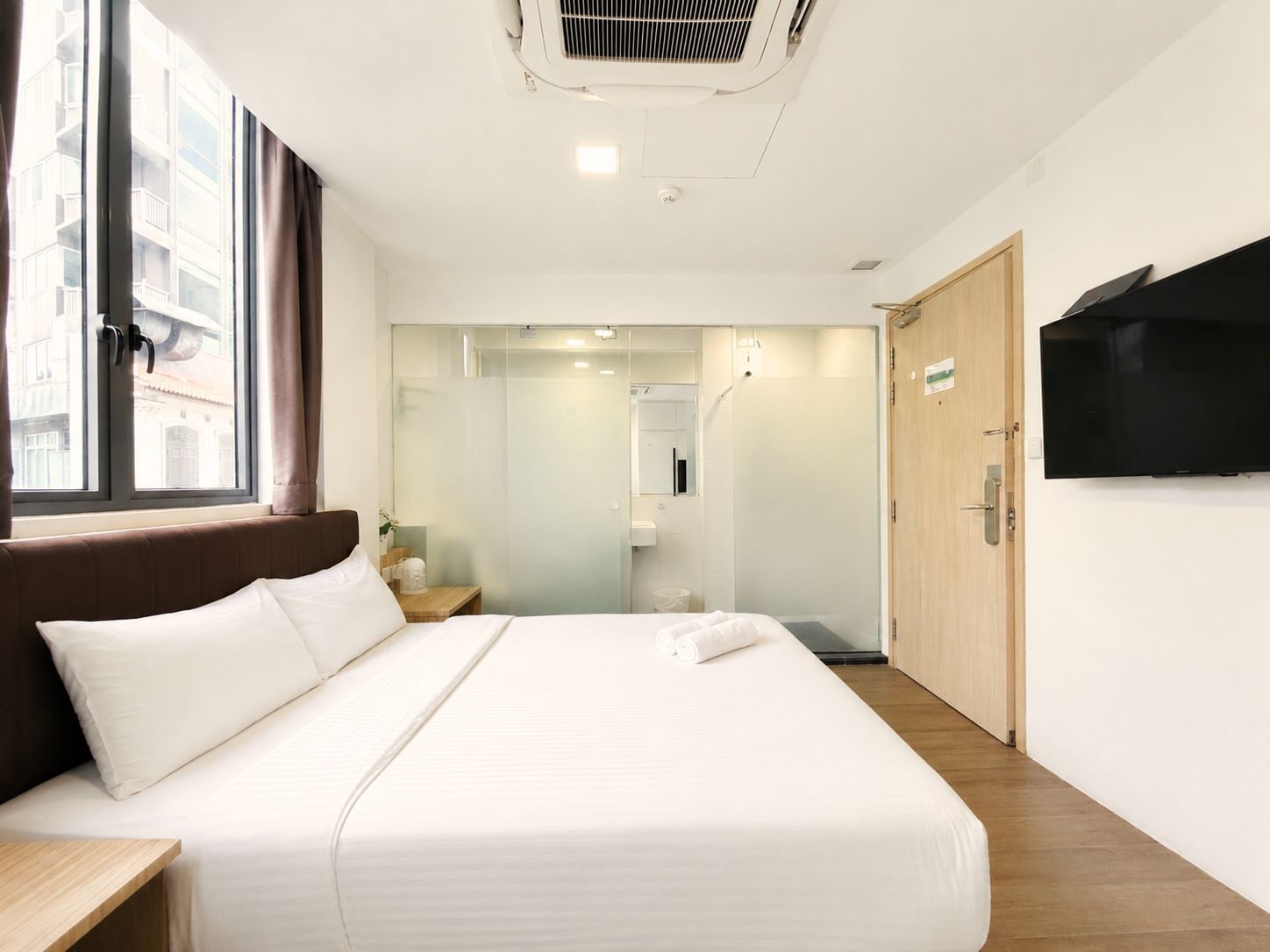 A hotel room with a bed, a television, a window, and a door.