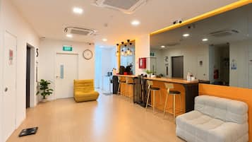 Una zona de recepción moderna con un mostrador de madera, taburetes de bar, un espacio de estar con un sofá y sillones, y un ascensor.