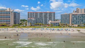 Un hotel sulla spiaggia con diversi edifici alti, una spiaggia sabbiosa e ombrelloni.
