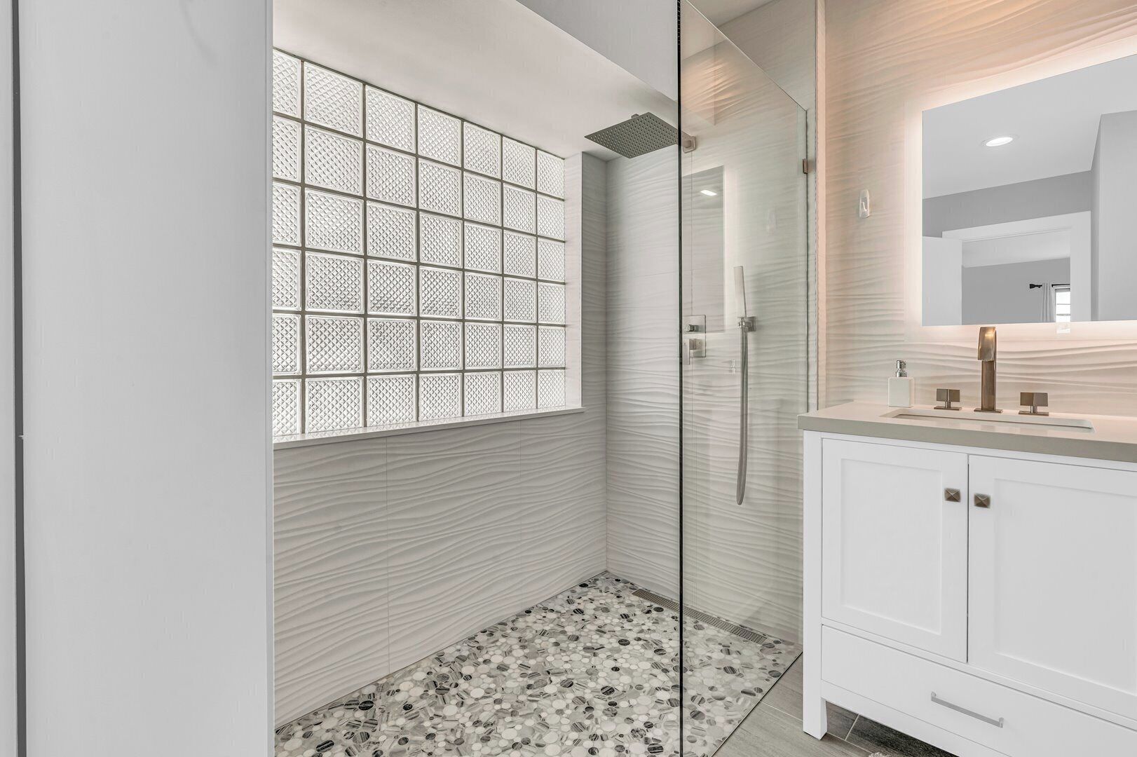 A modern bathroom with a glass shower enclosure, a patterned wall, and a tiled floor.