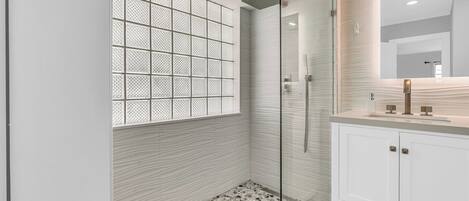A modern bathroom with a glass shower enclosure, a patterned wall, and a tiled floor.