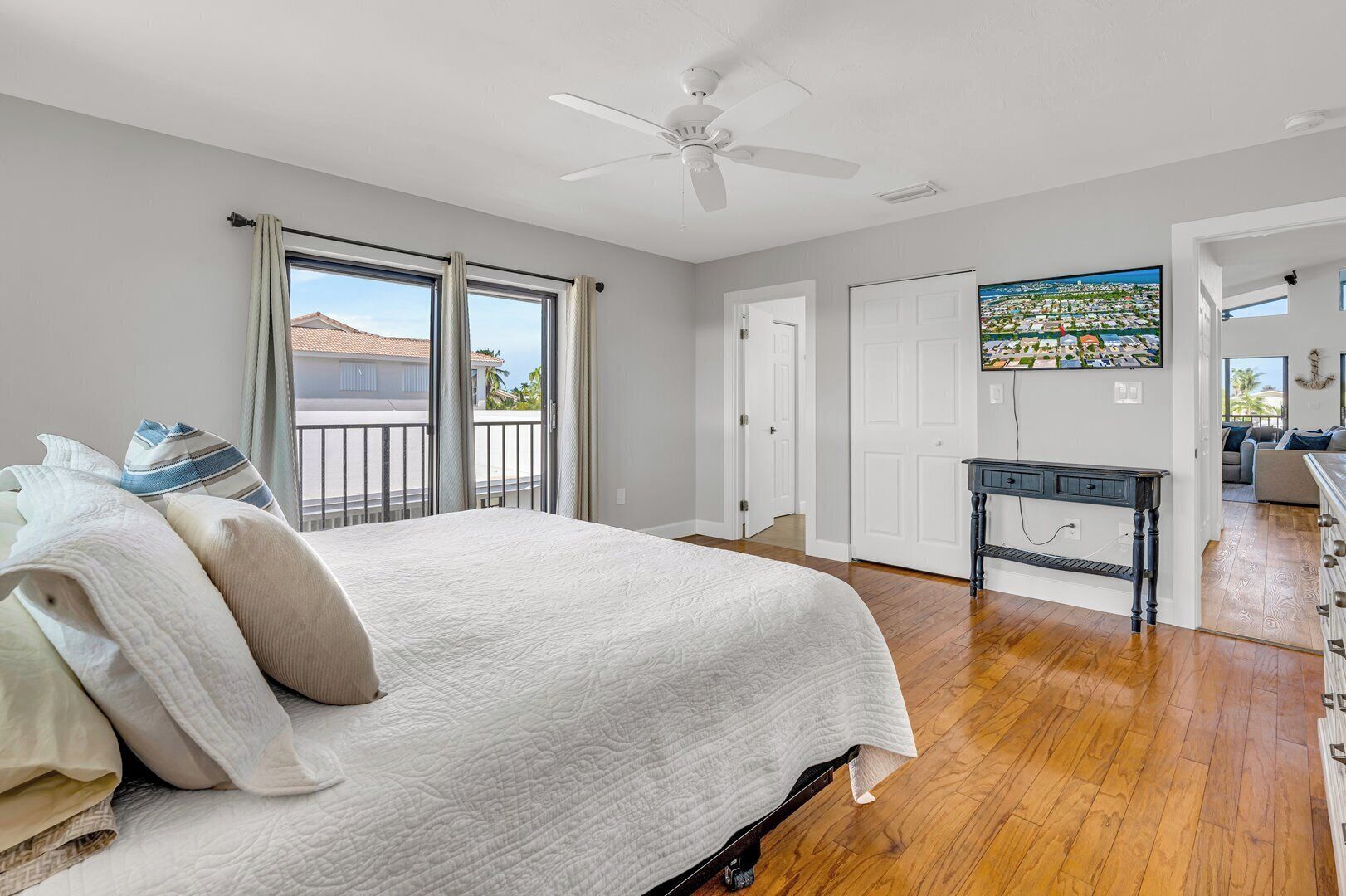 A bedroom with a bed, a ceiling fan, a window with curtains, a door, and a view of a cityscape through a TV screen.