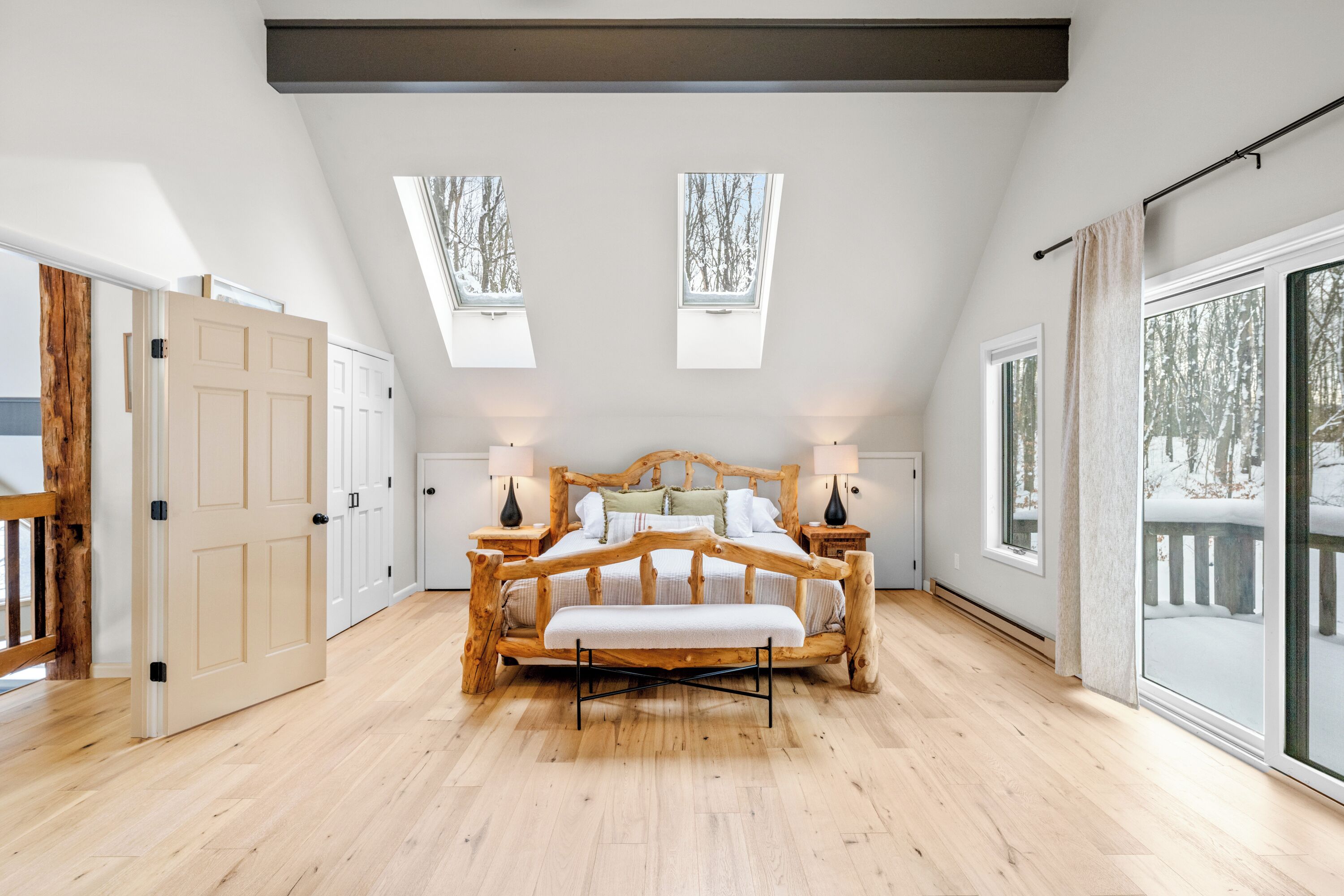 Ein Schlafzimmer mit einem hölzernen Bett, Dachfenstern, einem großen Fenster und einer Schiebeglastür zum Balkon.