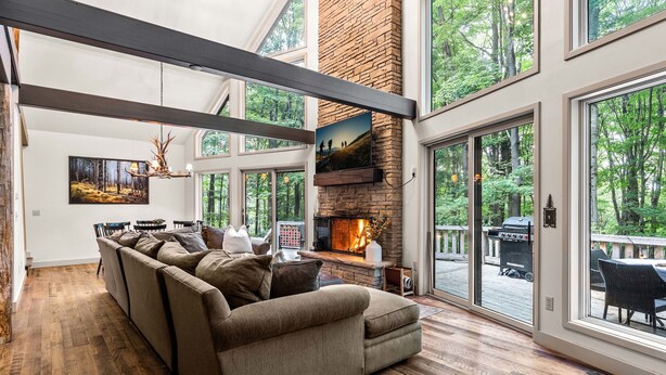 A spacious living room with a large sectional sofa, a fireplace, and large windows offering a view of the outdoors.