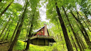 A cabin in a forest with a wooden deck and a chimney.
