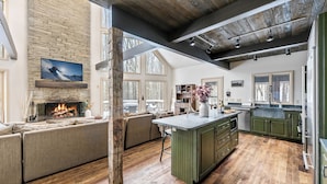 A spacious living room with a fireplace, a large window, and a kitchen with green cabinets.