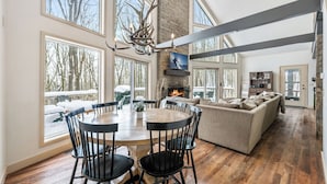 A spacious living room with a fireplace, large windows, and a dining area with a round table and chairs.