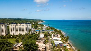 An aerial view of a coastal resort with high-rise buildings, a beach, and a clear blue sky. - Beautiful Oceanfront  2 bedroom, 2 bath condo Aguada, PR (Aguada)