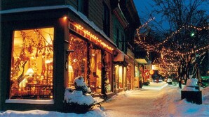 Una strada innevata con vetrine illuminate e un albero decorato con luci.