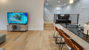 A modern kitchen with a wooden countertop, bar stools, and a TV on a wooden cabinet. - Downtown Stay in East Austin @ 12th Street (Austin)