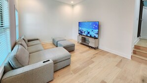 A modern living room with a sectional sofa, a flat-screen TV on a wooden stand, a ceiling fan, and a staircase leading to an upper level. - Downtown Stay in East Austin @ 12th Street (Austin)