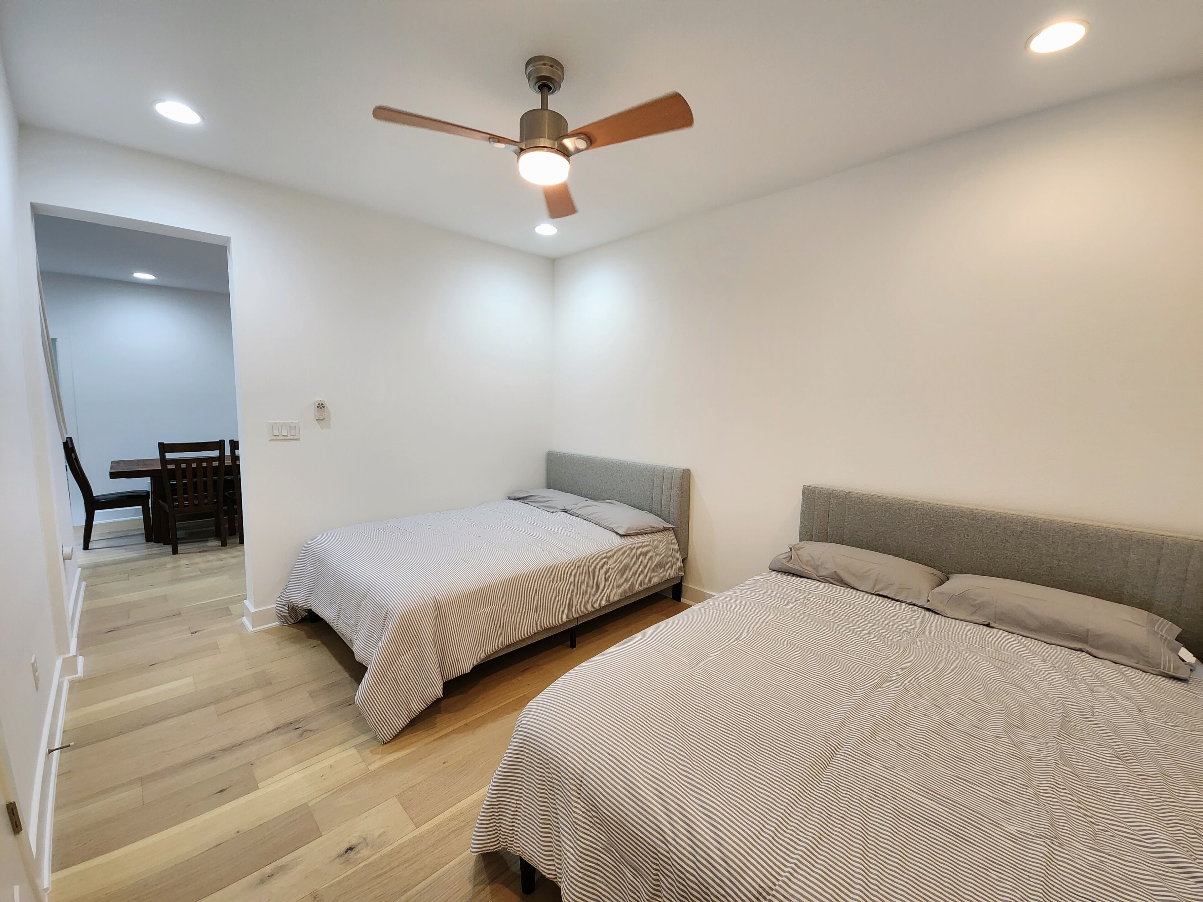 Quarto com duas camas, um ventilador de teto e um espaço de refeições com cadeiras e uma mesa.