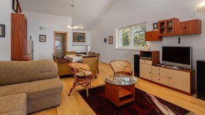 Ein modernes Wohnzimmer mit einer Couch, Sesseln, einem Glastisch, einem Fernseher und Holzschränken.