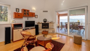 Ein Wohnzimmer mit Fernseher, Holzschränken, Korbstühlen und einem Kamin.