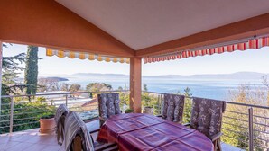 Ein Balkon mit Tisch und Stühlen, mit Blick auf ein Gewässer und ferne Hügel.