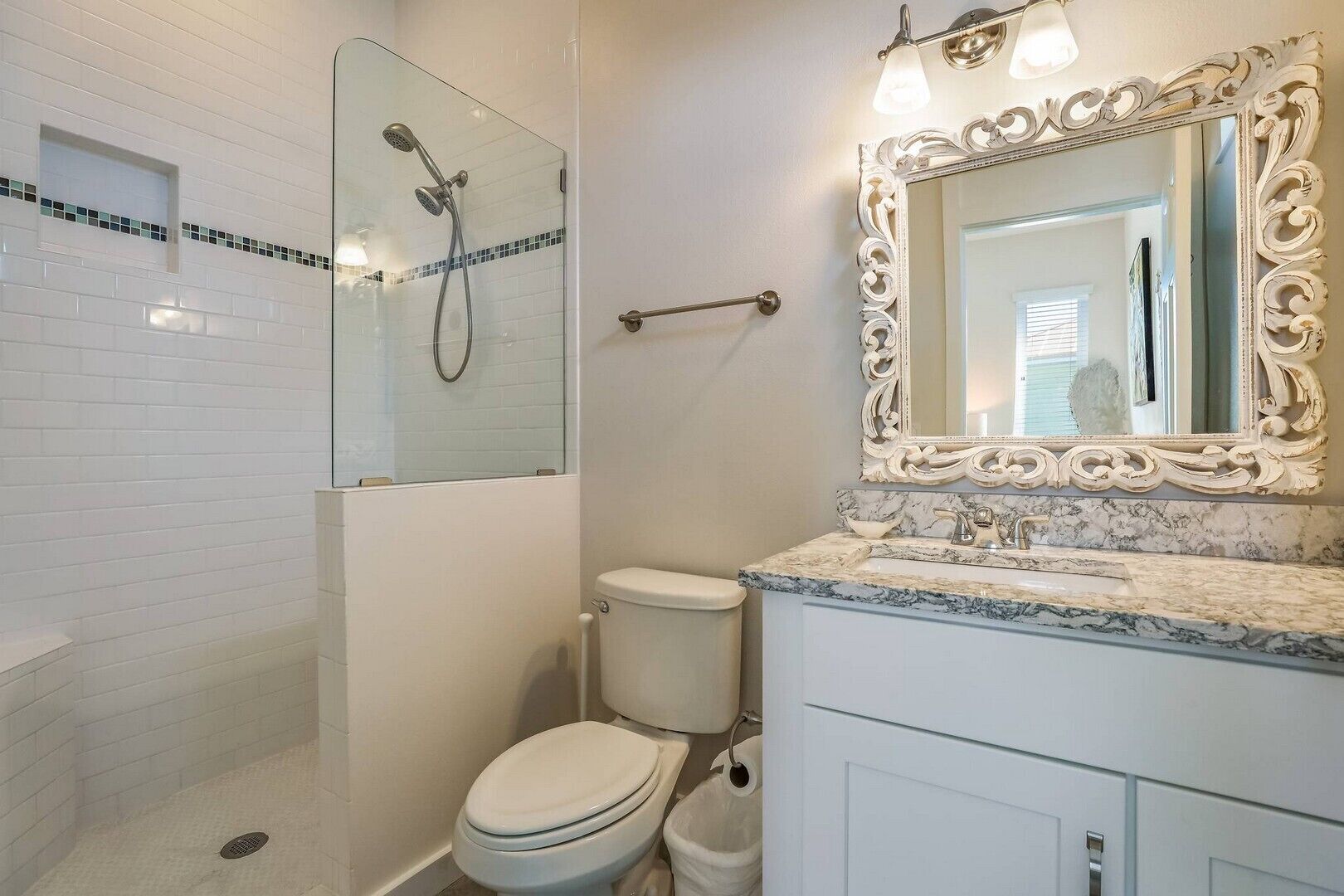 Un baño con ducha de vidrio, inodoro blanco, lavamanos de mármol y un espejo decorado.