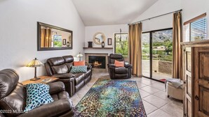 Un salón amplio con sofás de cuero, chimenea, un espejo grande y vistas a un paisaje montañoso a través de una puerta corrediza de vidrio.