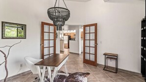 Un comedor con una mesa y sillas de madera, una araña y vista a la cocina.
