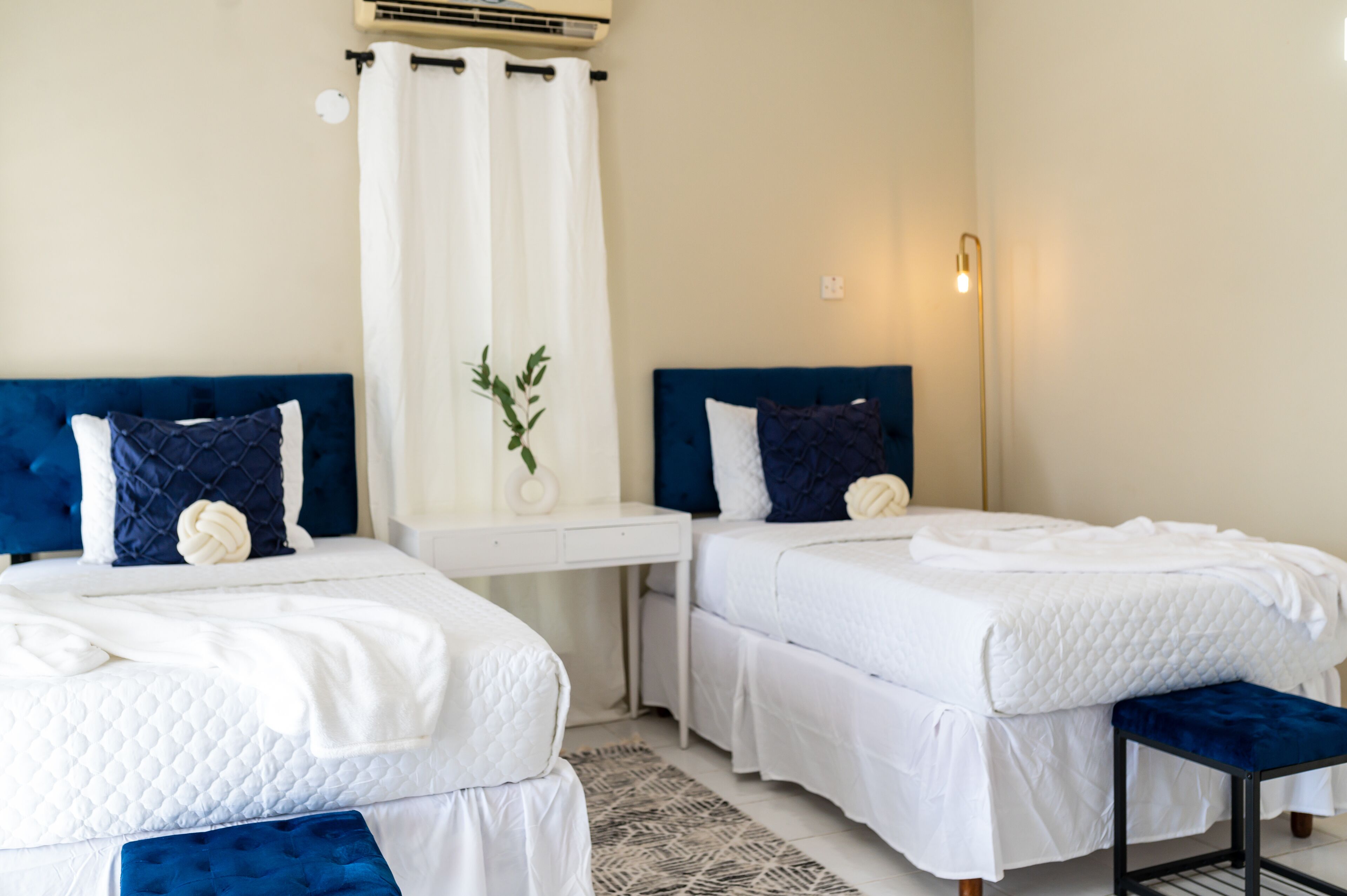 Habitación de hotel con dos camas, un escritorio blanco, una mesita pequeña y un banco.