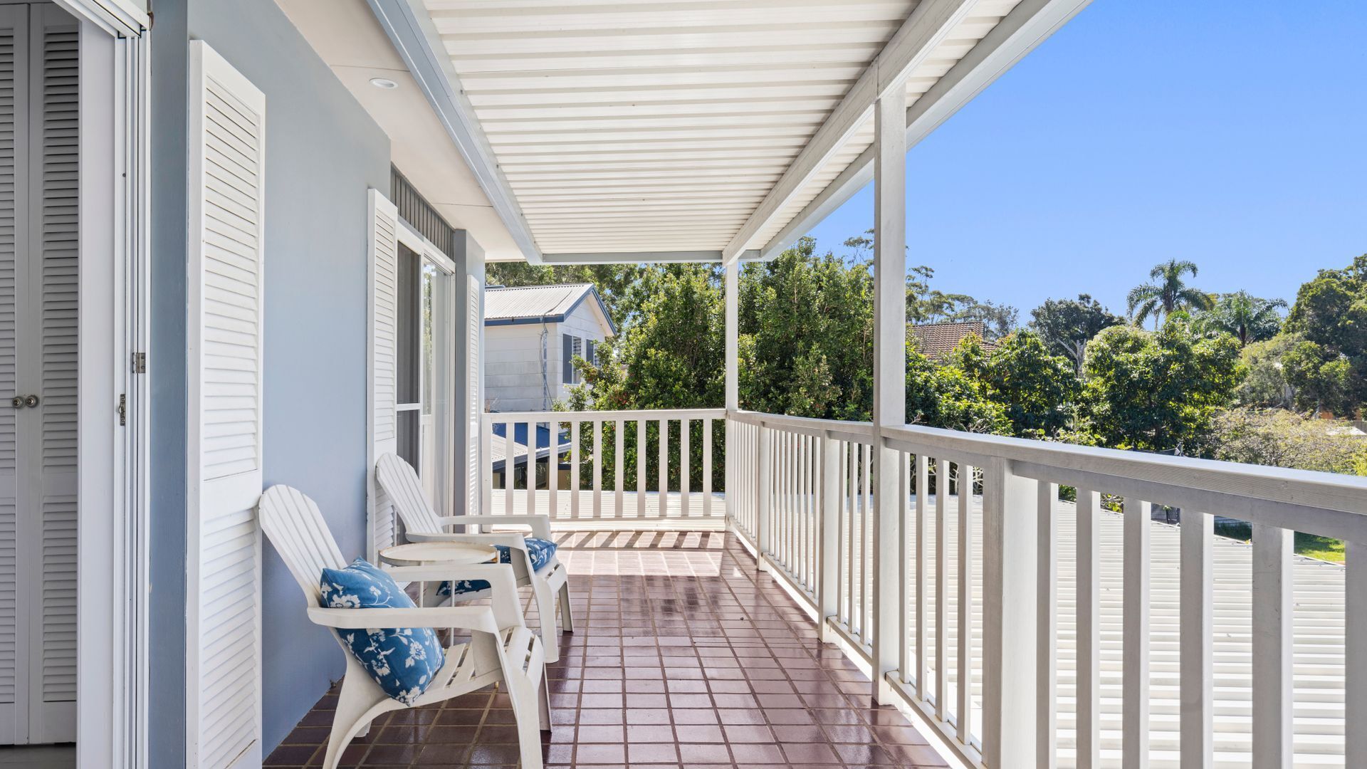 A covered porch with white railings and two white chairs with blue cushions.