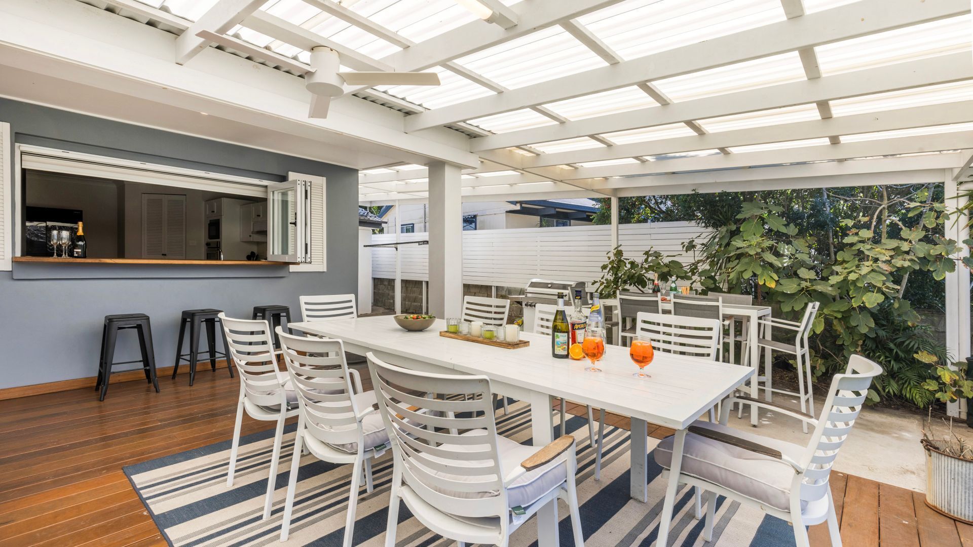 Eine Terrasse im Freien mit einem weißen Tisch und Stühlen, einem Grill und einer Bar.