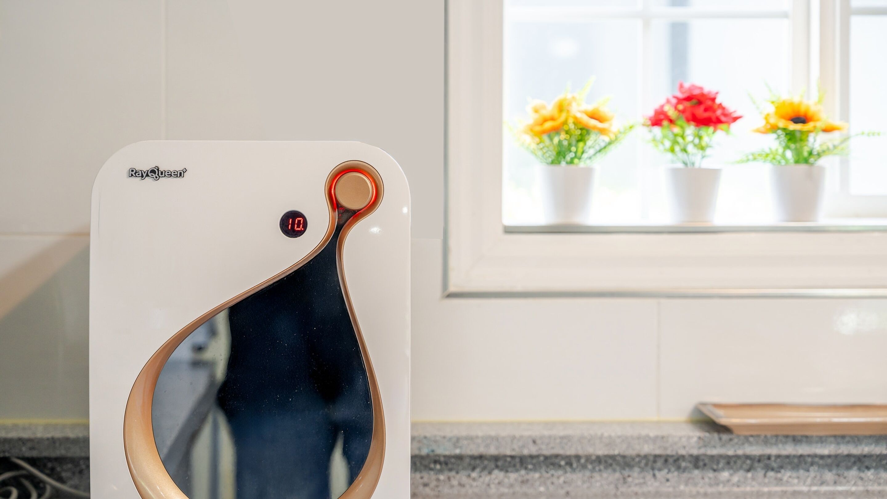 Eine Küche mit weißer Arbeitsplatte, einem Fenster mit Blumentöpfen und einer digitalen Waage, die die Zahl 10 anzeigt.