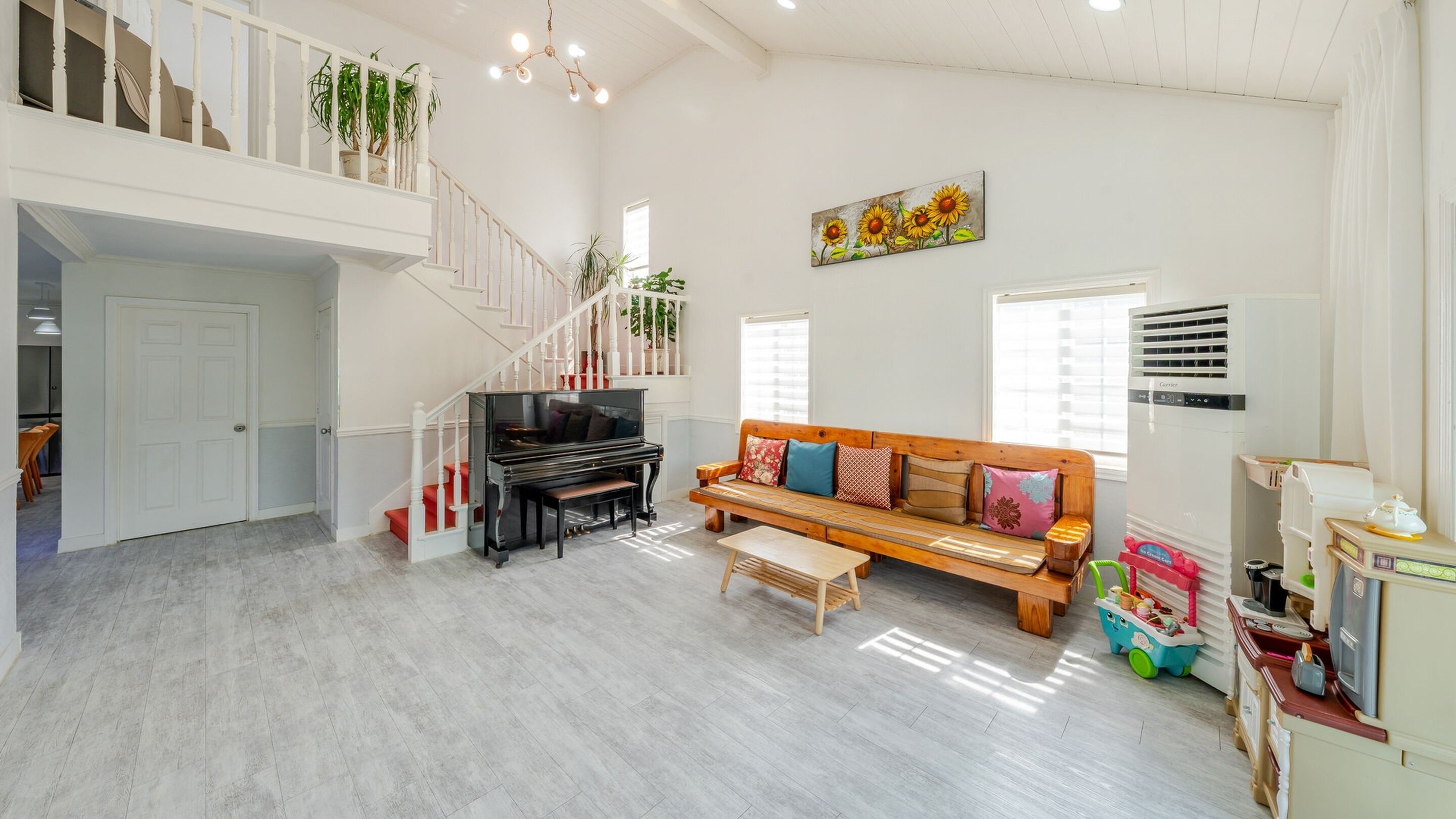 Amplia sala de estar con un piano, un sofá, una escalera y una zona de cocina con un juego de cocina para niños.