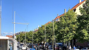 En smal vattenväg med båtar förtöjda på båda sidor, en gångväg för fotgängare och byggnader i bakgrunden.