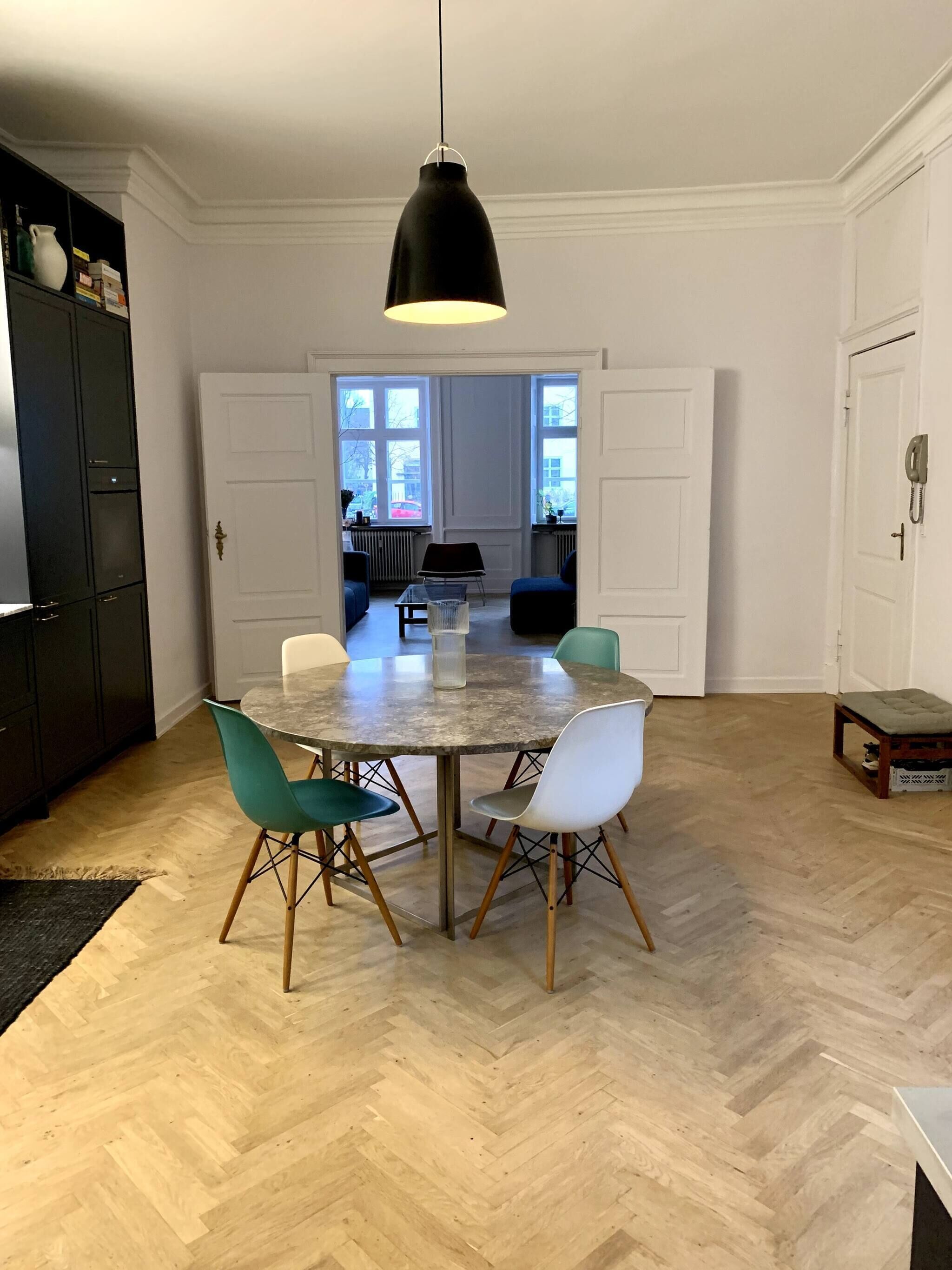 A dining area with a round table, four chairs, and a hanging light fixture.