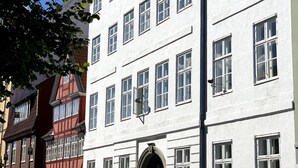 En byggnad med flera våningar, en vit fasad, många fönster och en central entré med en svart dörr.