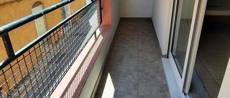 A narrow balcony with a metal railing, a tiled floor, and a clear view of a building in the background.