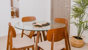 Un coin repas comprenant une table ronde en verre, des chaises en bois, un luminaire suspendu, une porte en bois et une plante en pot.