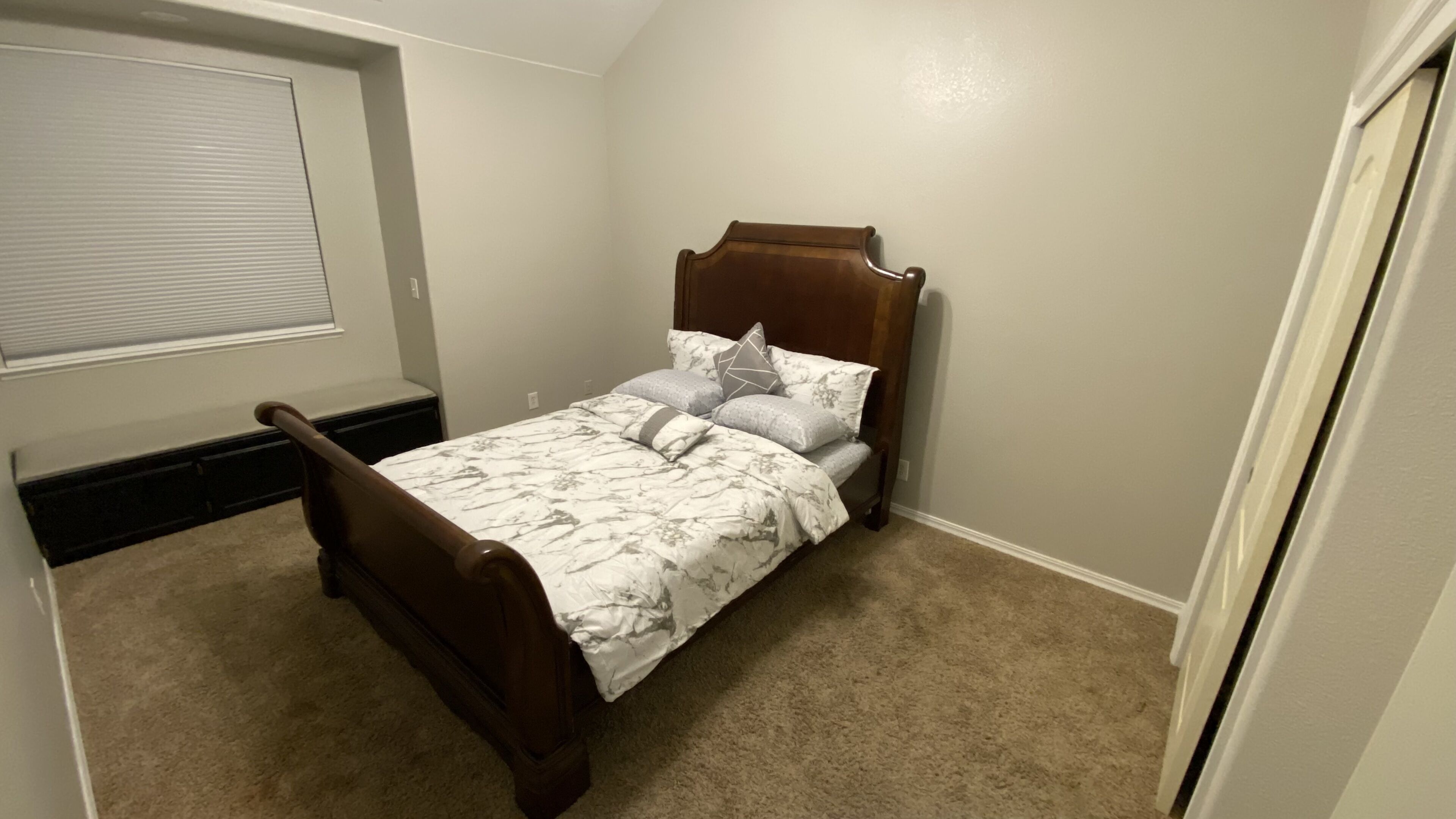 Une chambre avec un lit simple, une fenêtre avec des stores et un sol recouvert de moquette.
