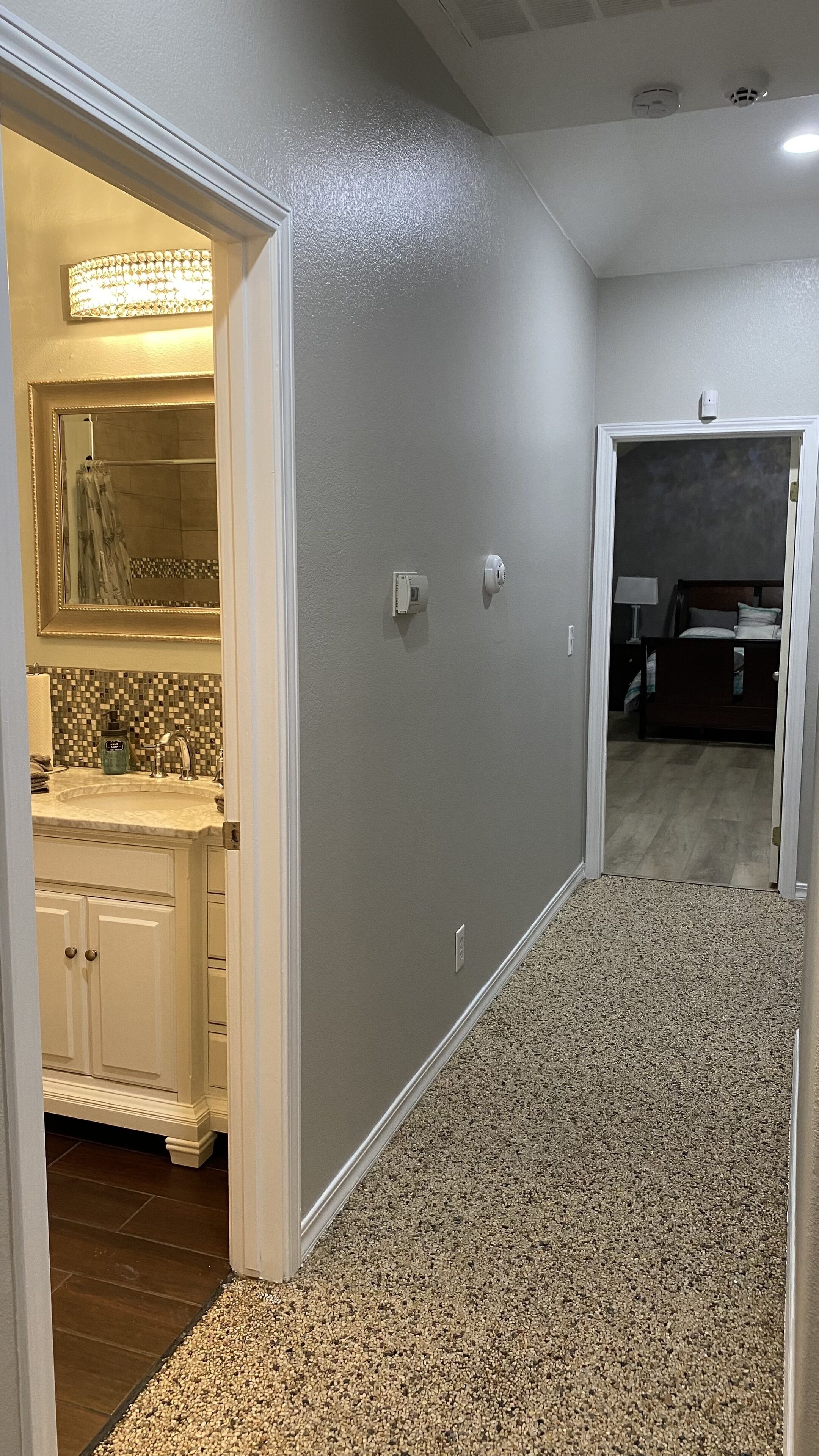 A hallway with a bathroom on the left, a bedroom on the right, and a carpeted floor.