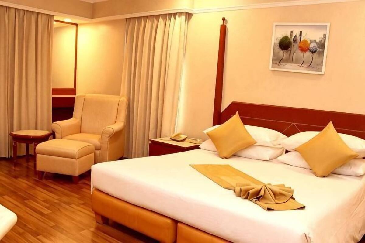 A hotel room with a large bed, a chair, a nightstand, and a painting on the wall.
