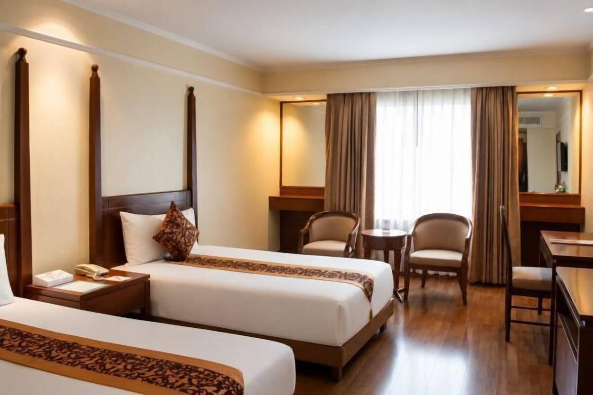 A hotel room with two beds, a desk, a chair, a small table, and a mirror.