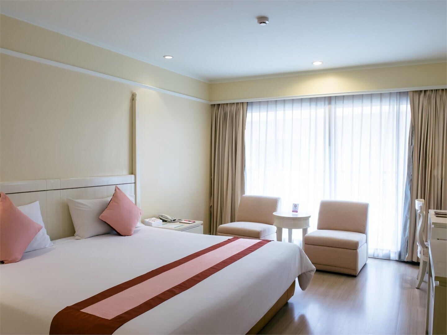 A hotel room with a large bed, two armchairs, a small table, and a desk with a chair.